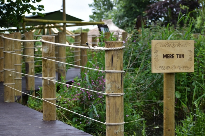 The entrance to the Mere Tun at WWT Martin Mere. There is a 'Mere Tun' sign welcoming visitors, and a boardwalk that leads up to the village.